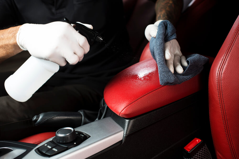 A close-up of a car detailing worker cleaning the interior using a microfiber cloth.