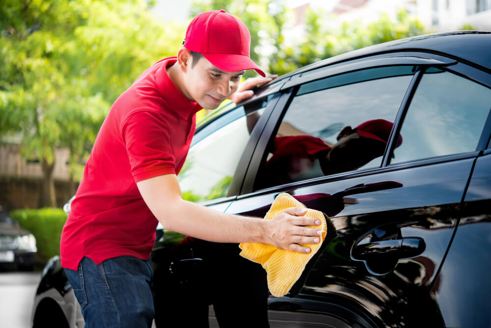 Auto service staff in red uniform cleaning car with microfiber cloth.