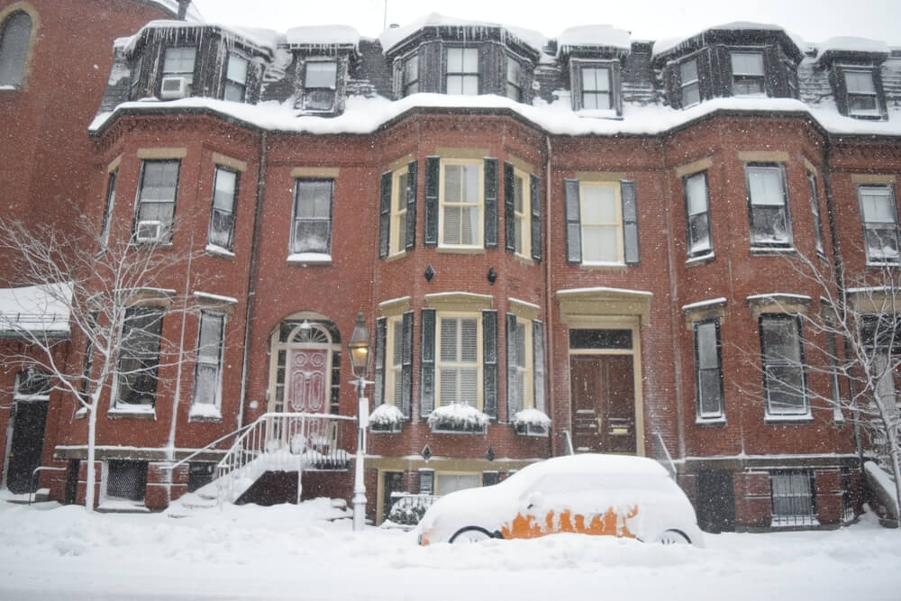 A car covered in snow in front of old buildings in Boston.