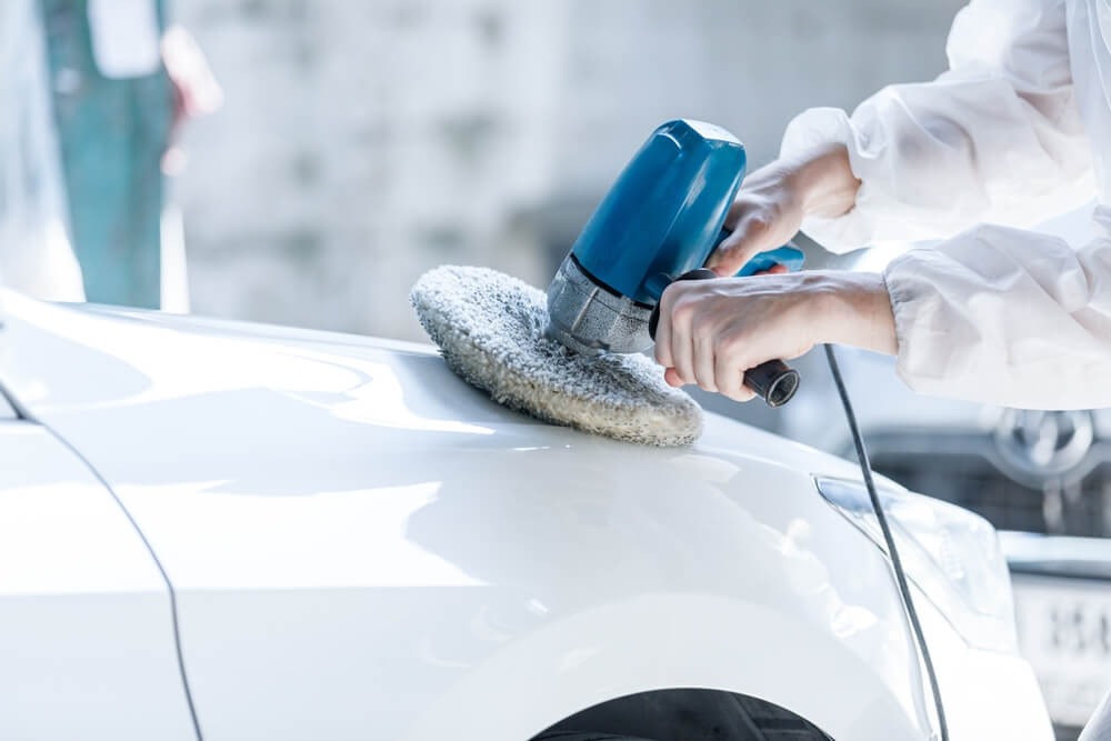 Close-up shot of a professional car painter repairing scratches and damaged car painting.