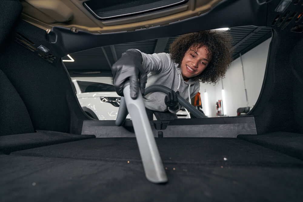 Joyful auto detailer vacuum-cleaning a car interior.